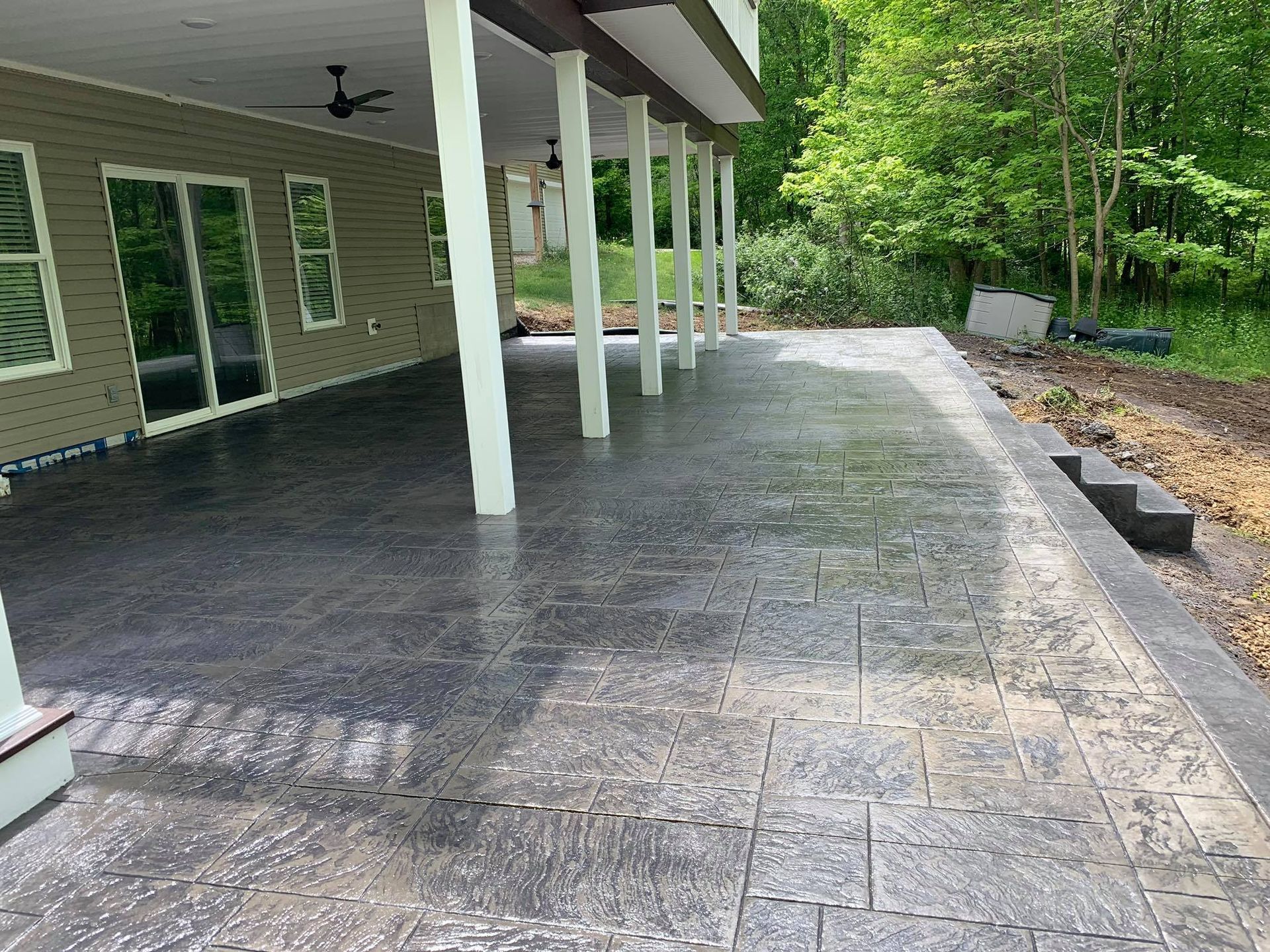 A large concrete patio with a ceiling fan in front of a house.