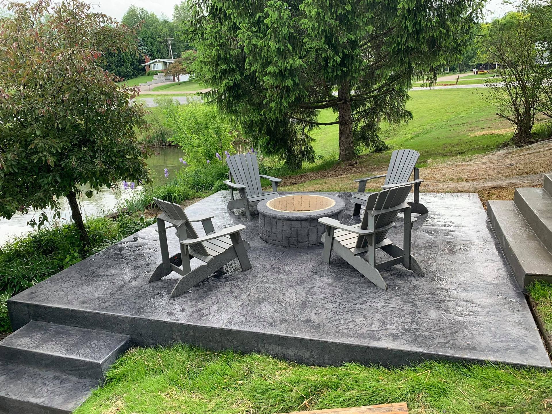 A fire pit is sitting on top of a concrete patio with chairs.