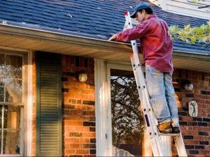 A man is standing on a ladder working on the roof of a house.