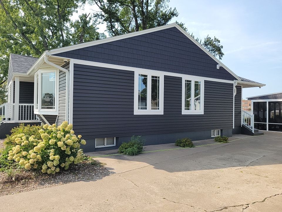 A house with a black siding and white trim is for sale.
