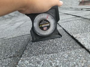 A person is holding a measuring device over a roof.