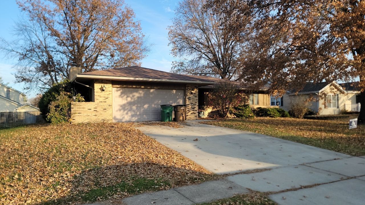 A house with a driveway filled with leaves and trees in the background.