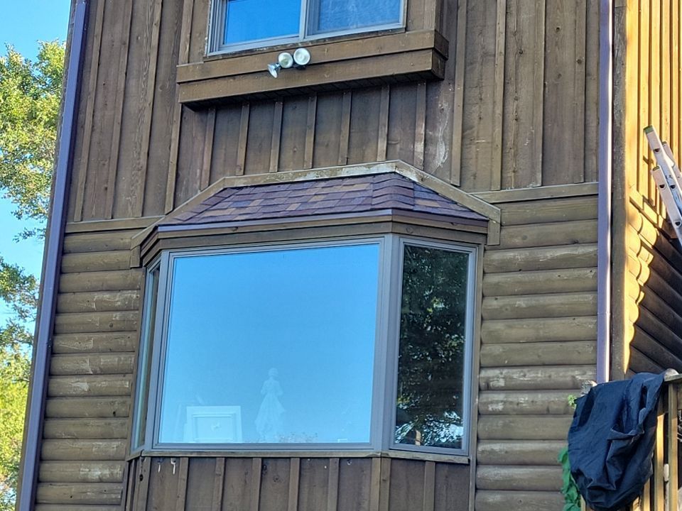 A log cabin with a large bay window and a ladder on the side.