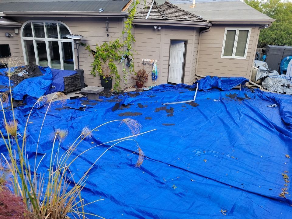 A large blue tarp is covering the ground in front of a house.