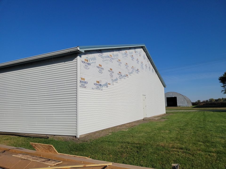 A large white barn is sitting in the middle of a grassy field.