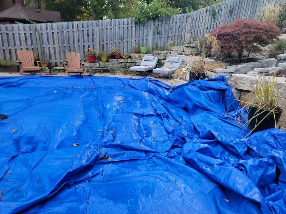 A blue tarp is covering a swimming pool in a backyard.