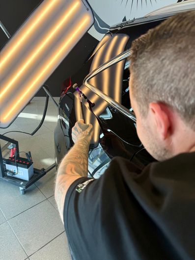Ein Mann arbeitet an einem Auto, hinter ihm ist ein Licht.