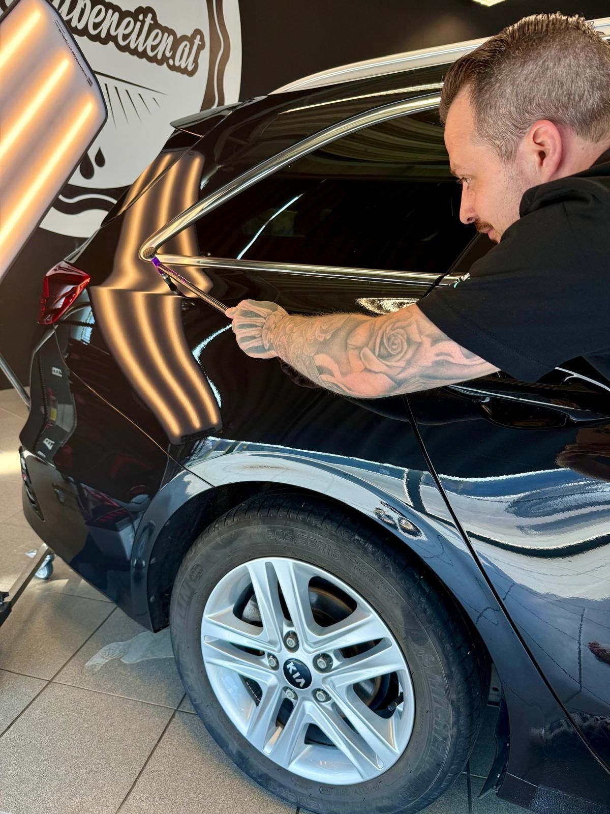 Ein Mann arbeitet am Kotflügel hinten eines schwarzen Autos.
