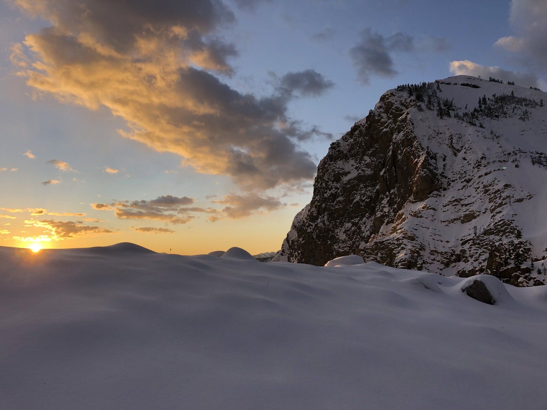 Snowy mountain and landscape at sunset with golden clouds and blue sky.