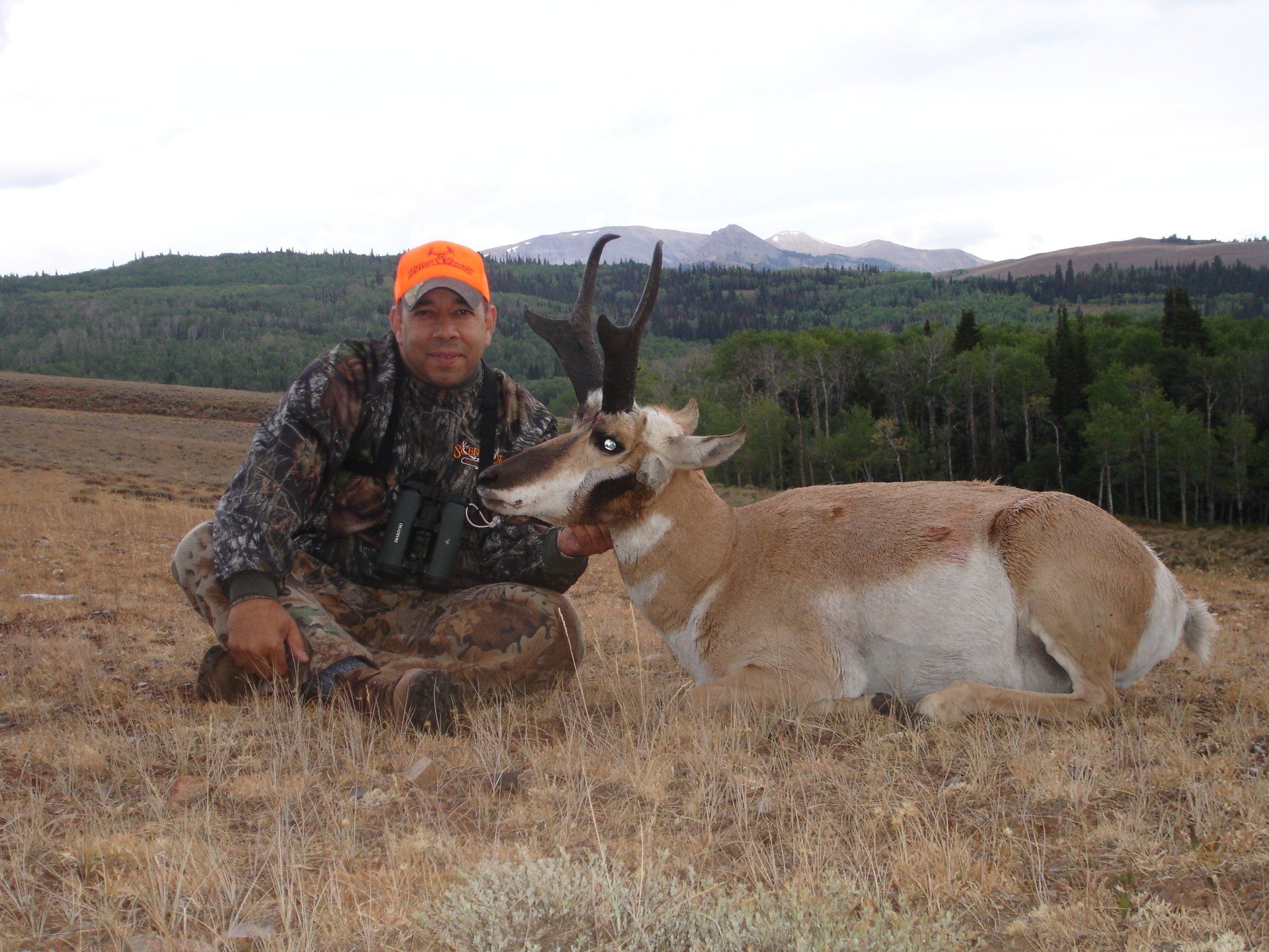 A man kneeling next to a deer with mountains in the background