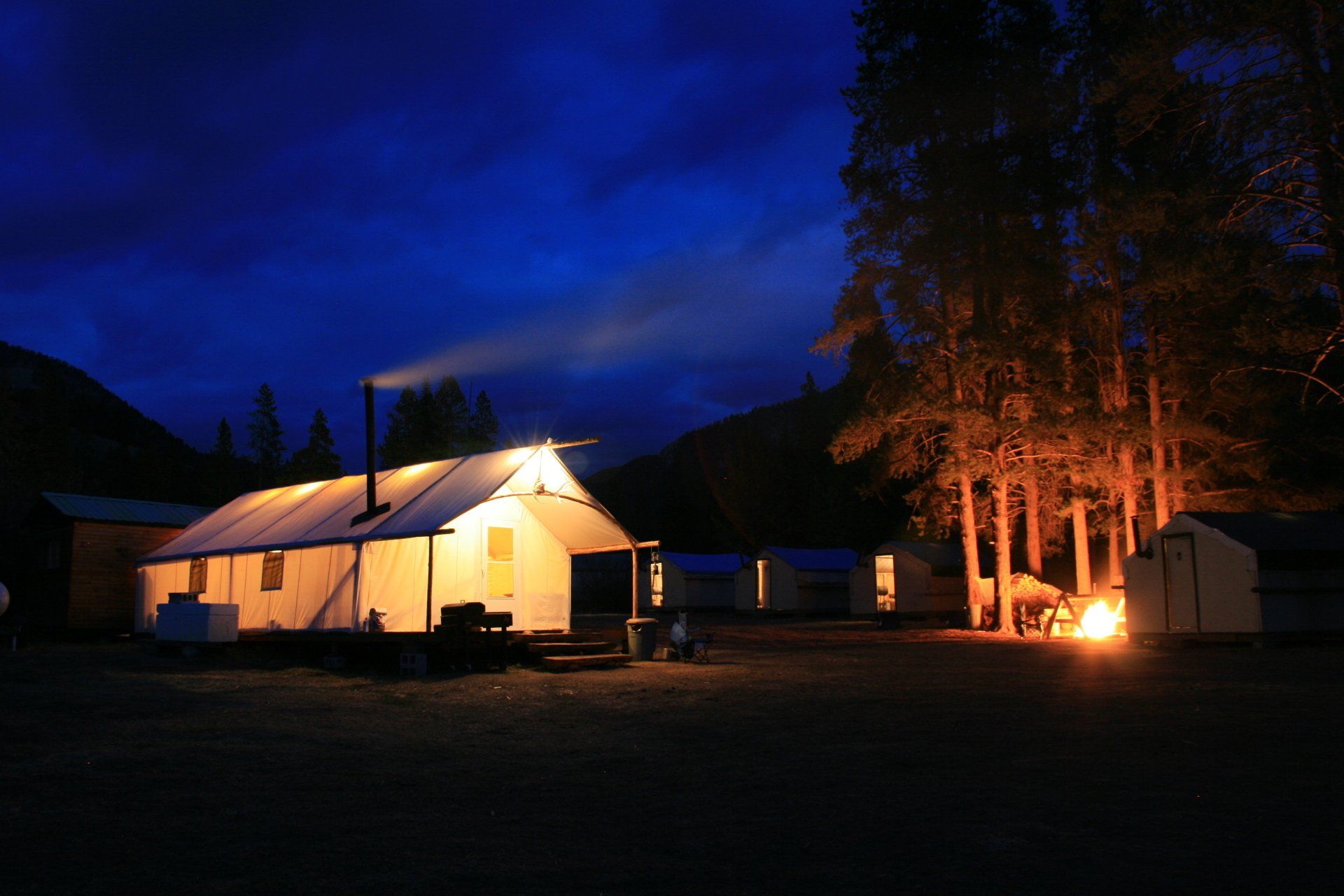 A tent is lit up at night with trees in the background
