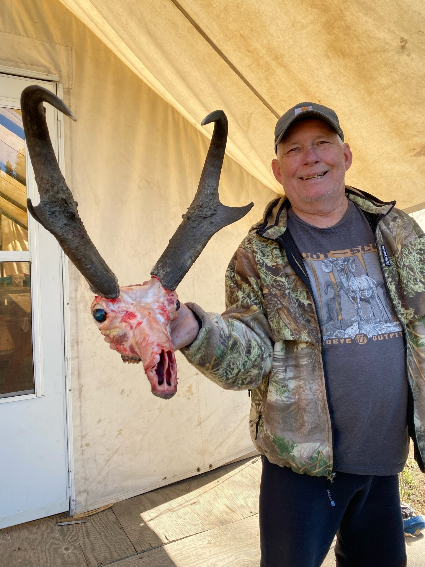A man in a camouflage jacket is holding a deer skull
