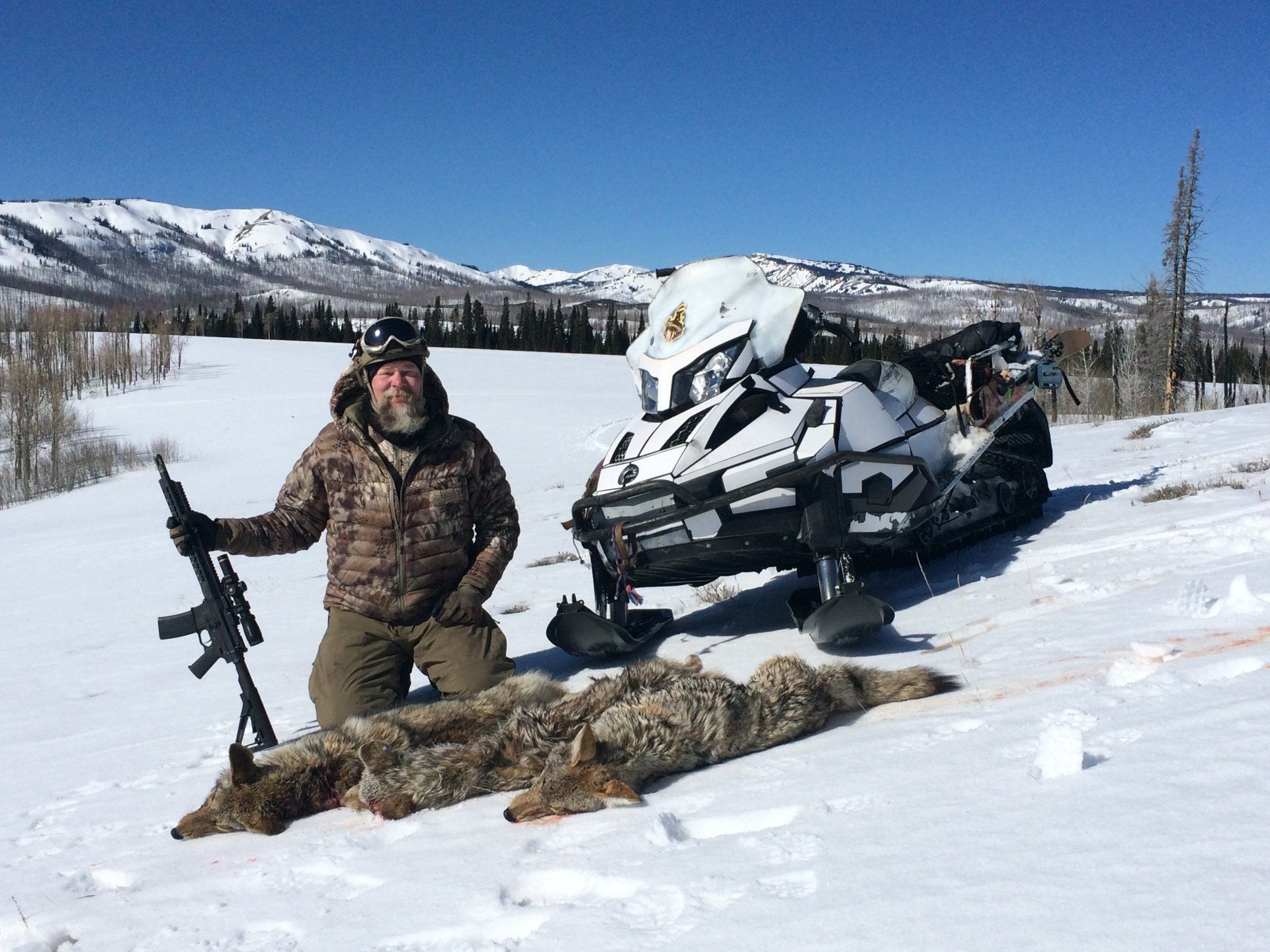 A man kneeling in the snow next to a snowmobile