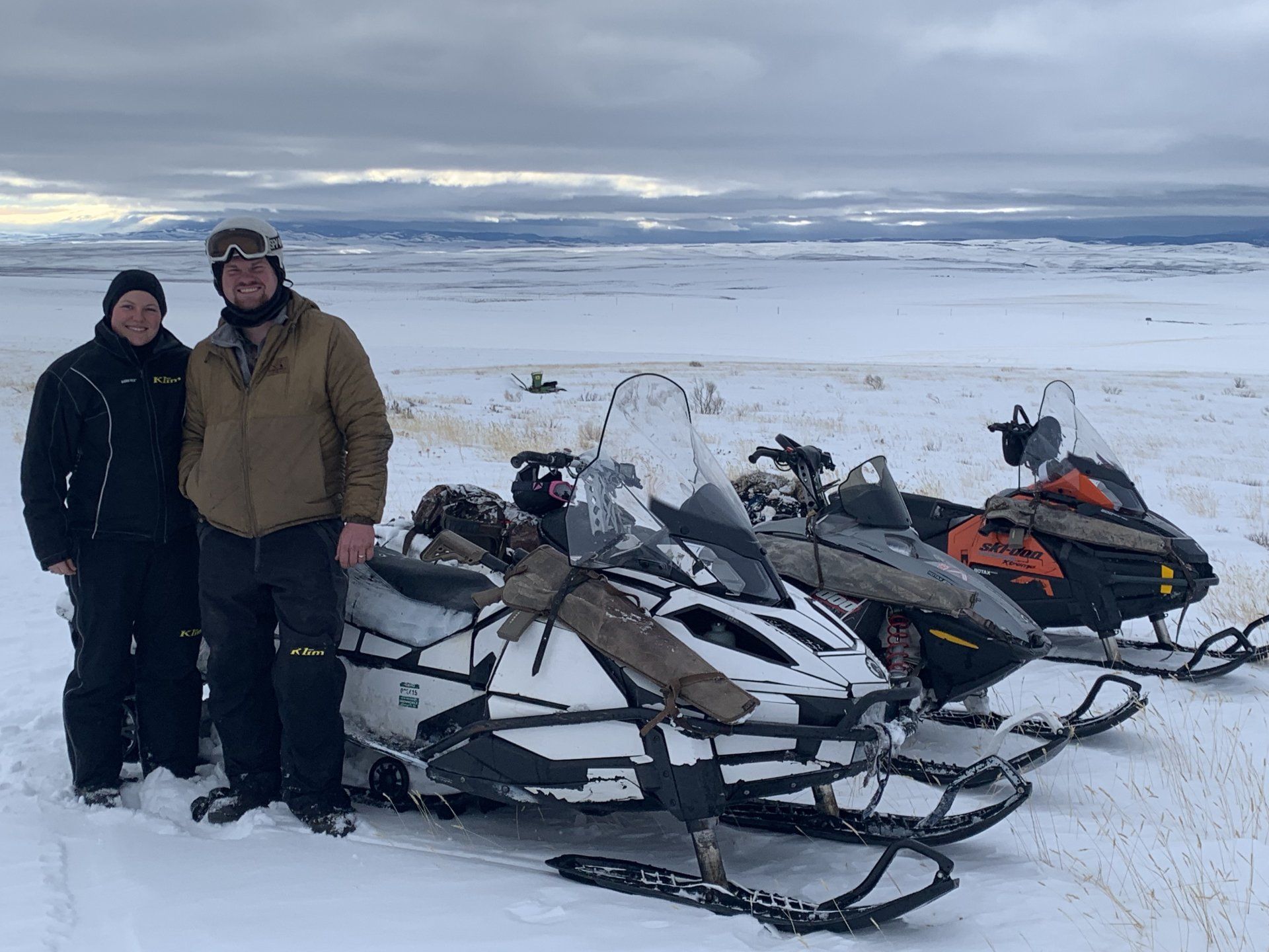 Two men standing next to snowmobiles in the snow