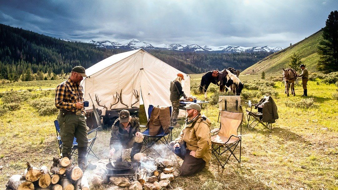 A group of men are sitting around a campfire in a field