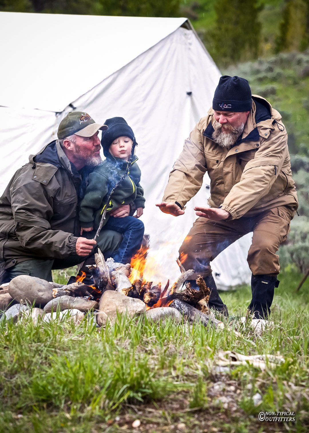 Two men and a child are sitting around a campfire