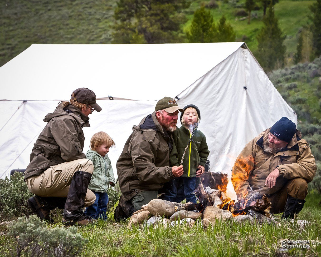A group of people sitting around a campfire in front of a tent