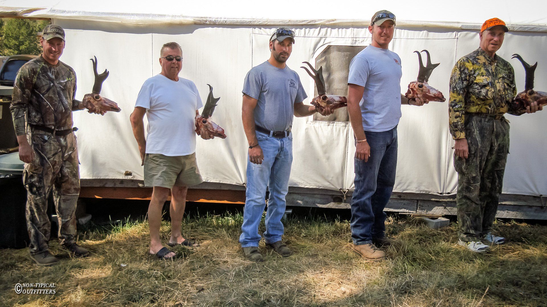 A group of men standing in front of a trailer holding trophies
