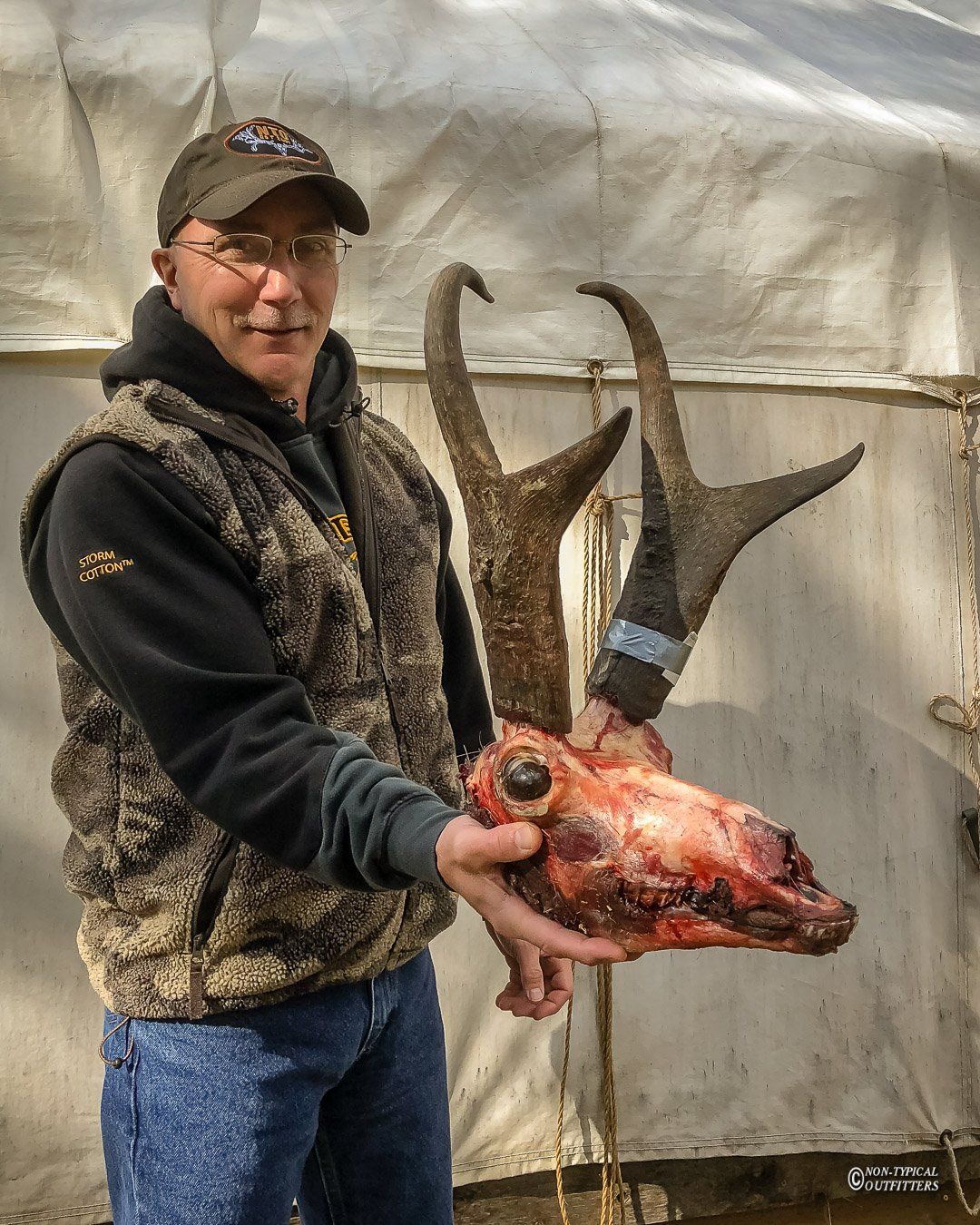 A man in a camo vest holds a deer skull