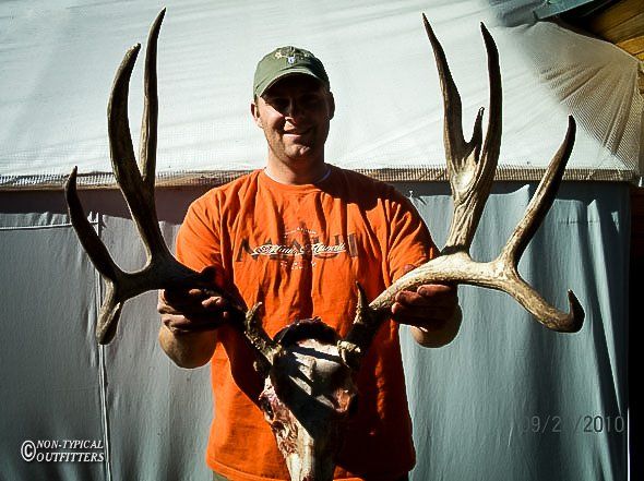 A man in an orange shirt is holding a large deer skull