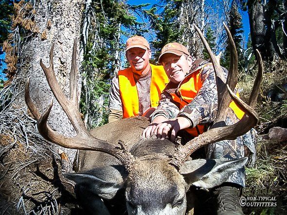 A couple of hunters posing with a large deer