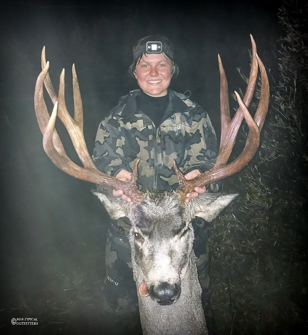 A woman in a camo jacket is holding a large deer