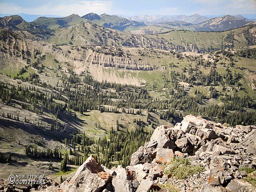 A vast mountain landscape with green valleys and rocky peaks under a bright sky.