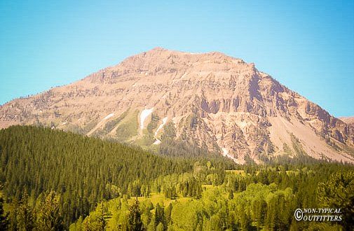 A large mountain with brown and rocky slopes, rising above a forest of green trees.