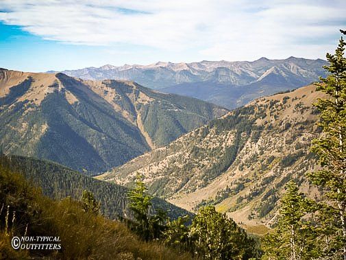 Mountain range with lush green valleys and peaks under a blue sky with some clouds.