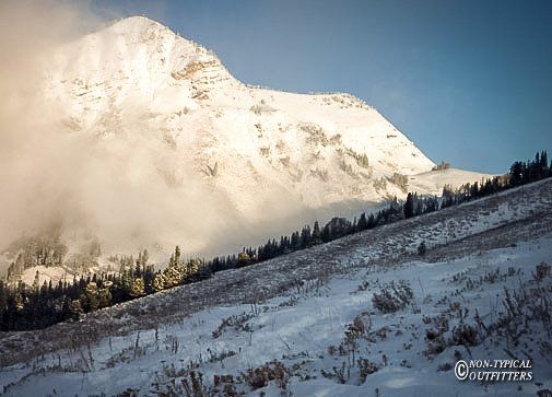 Snow-covered mountain peak with a sunlit slope and patches of clouds.