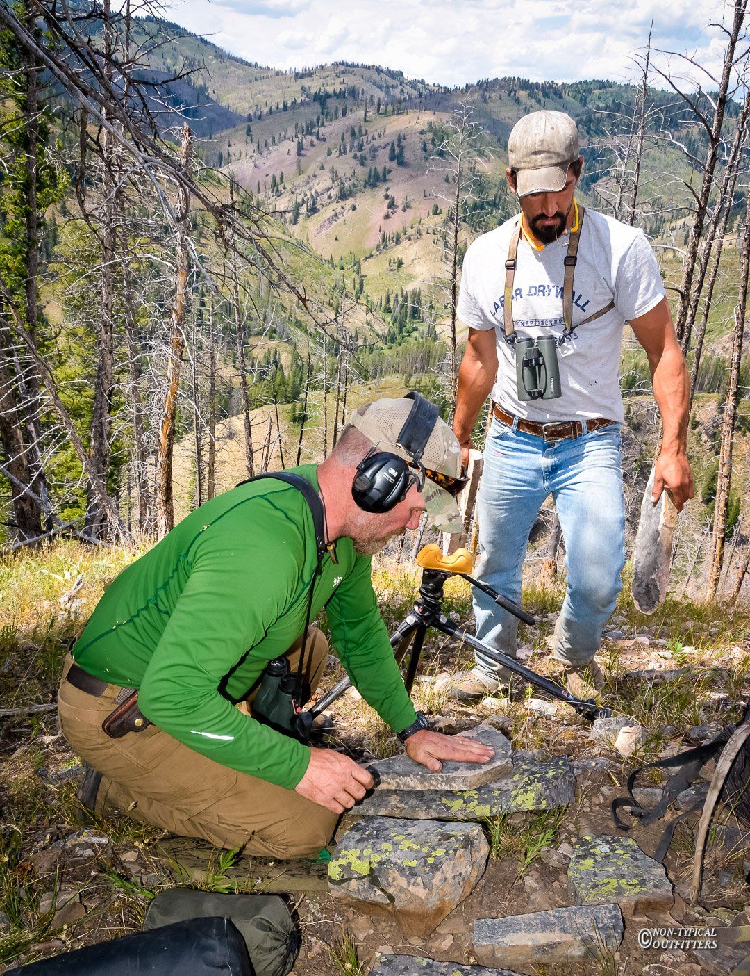 A man wearing headphones is kneeling down next to another man