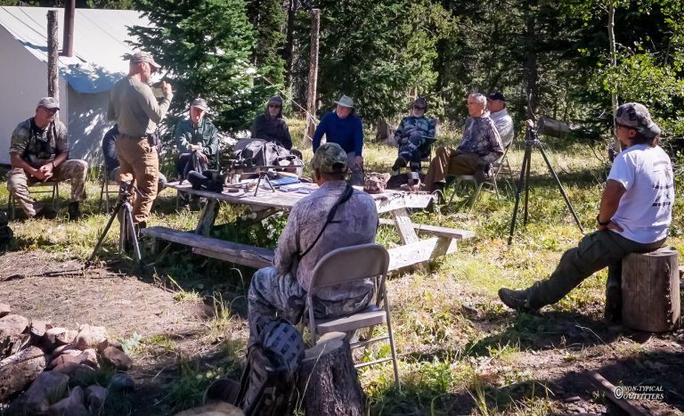 A group of people are sitting around a picnic table in the woods