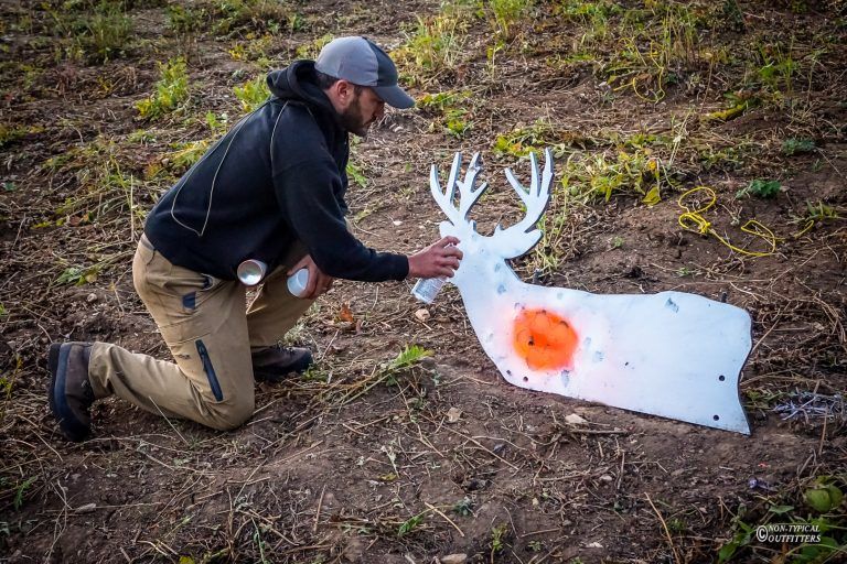 A man is kneeling down in front of a deer target.