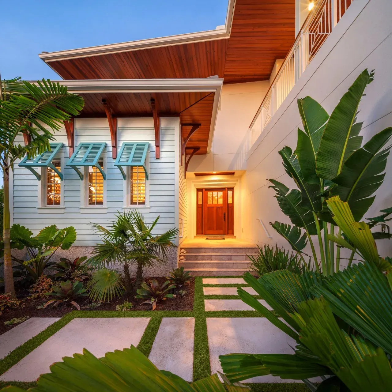 Tropical house exterior with light blue siding, wooden accents, and lush landscaping.