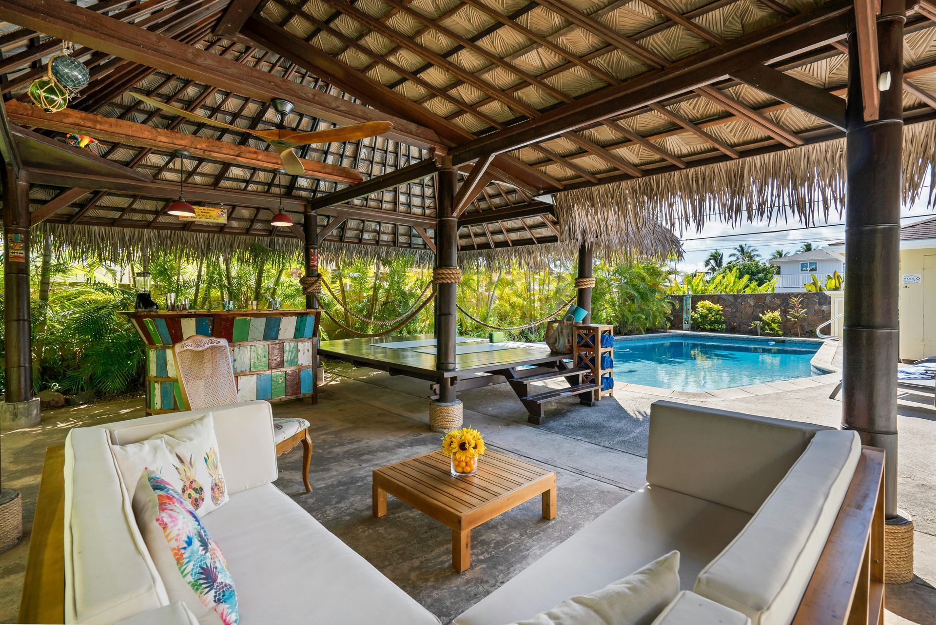 Outdoor lounge with thatched roof, white couches, pool in the background.
