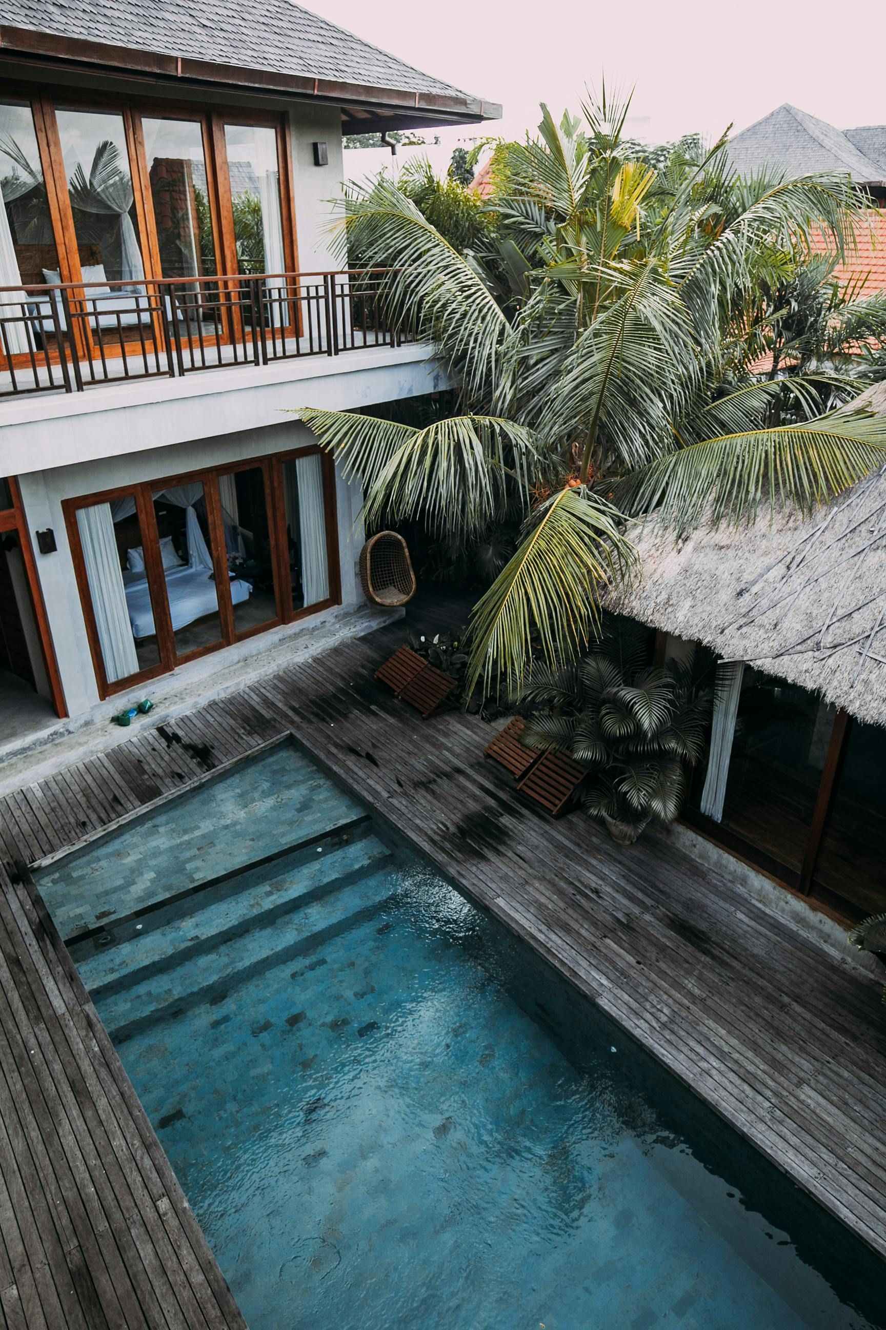 Overhead view of a villa with a pool, wooden deck, and tropical foliage; second-floor balcony.