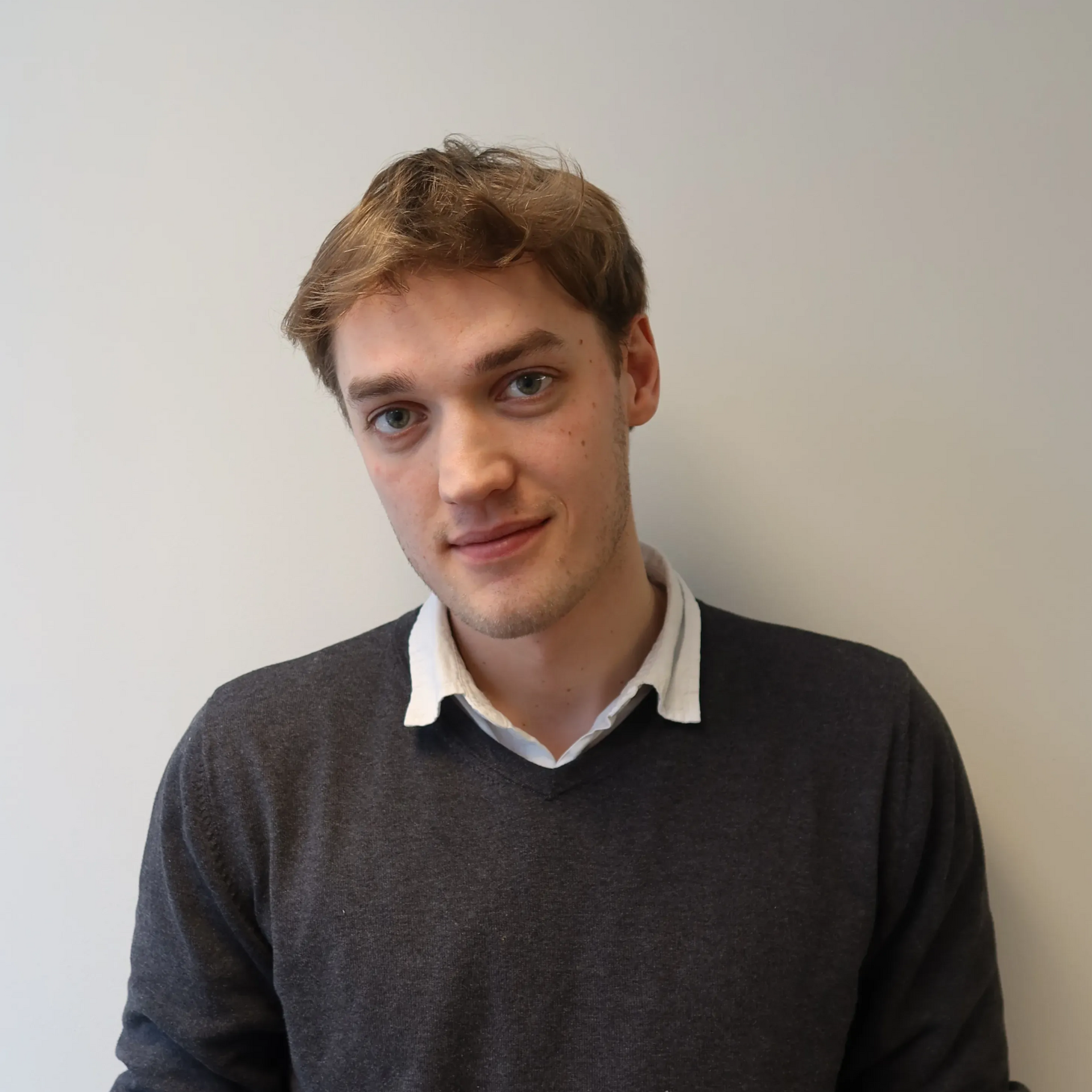 Bendik Grieg Skjold  med lys hud og brunt hår iført en hvit polotrendgenser, mot en hvit vegg.