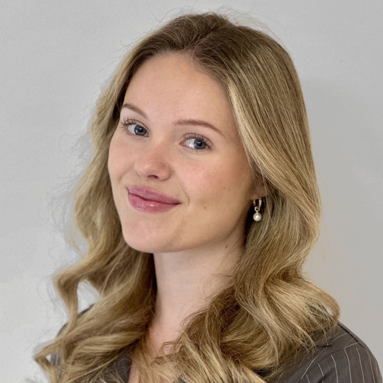 Blonde woman with wavy hair smiles at the camera; neutral background.