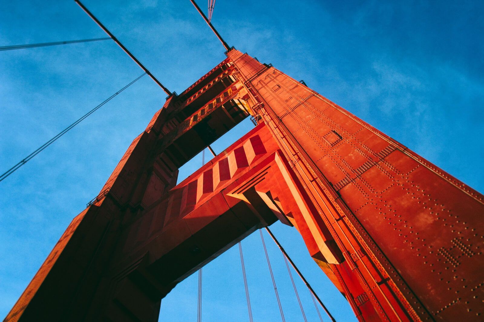 Golden Gate Bridge tower against a clear blue sky, viewed from below.