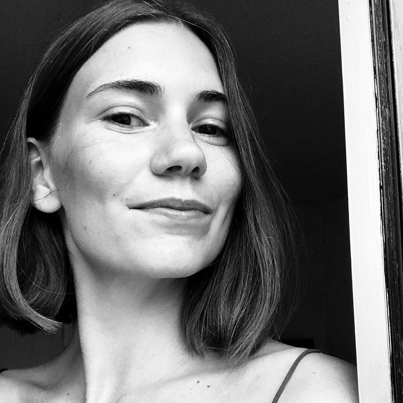 Woman with short hair smiling, leaning against a doorway, in black and white.