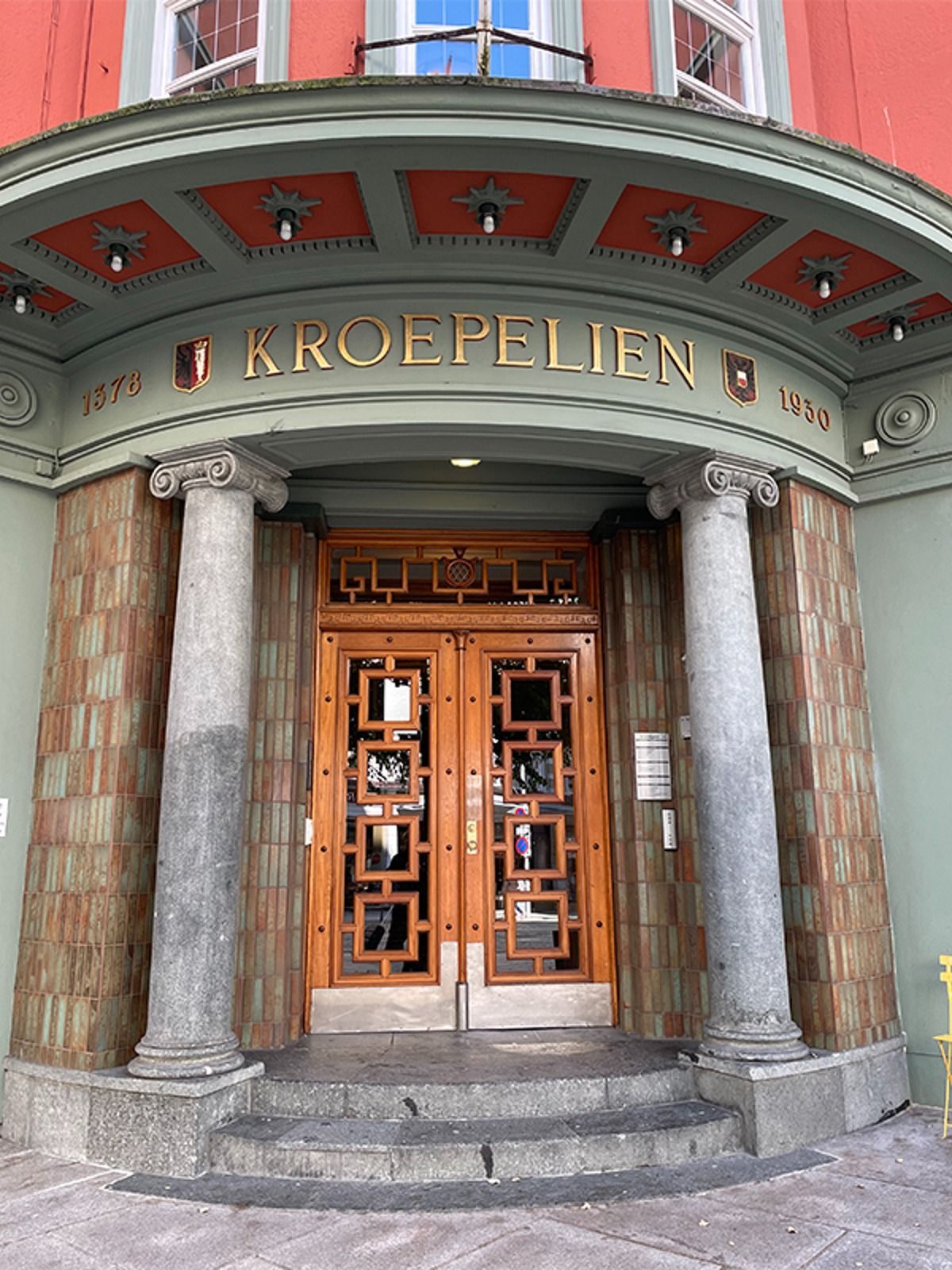Entrance of Kroepelien building with wooden doors, columns, and green/red accents.