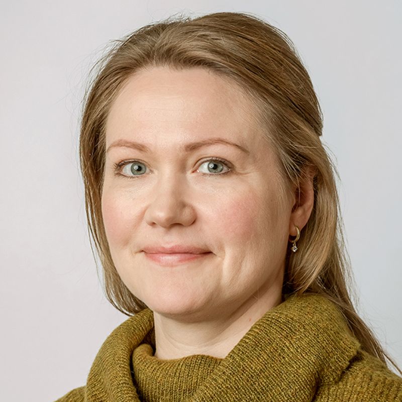 Woman with blonde hair, green eyes, and a light brown sweater smiles at the camera.