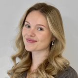Blonde woman with wavy hair smiles at the camera; neutral background.