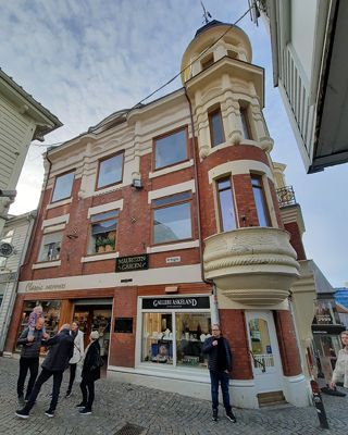Brick building with tower and shop fronts on a cobblestone street. People are in front of the building.