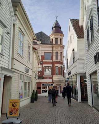 Narrow cobblestone street lined with white buildings, people walking toward a red brick building with a tower.