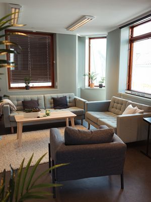 Living room with light blue walls, gray couches, and windows with brown blinds.