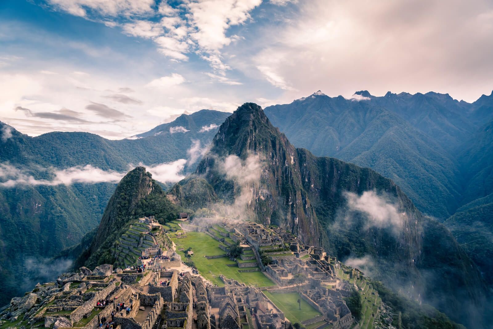 Machu Picchu mountain citadel, Peru. Stone ruins in a lush green valley, surrounded by towering, misty mountains.