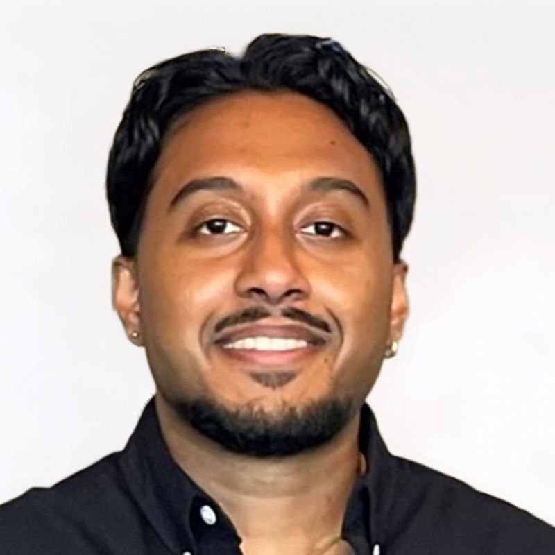 Man with dark hair and beard smiling, wearing a black shirt.