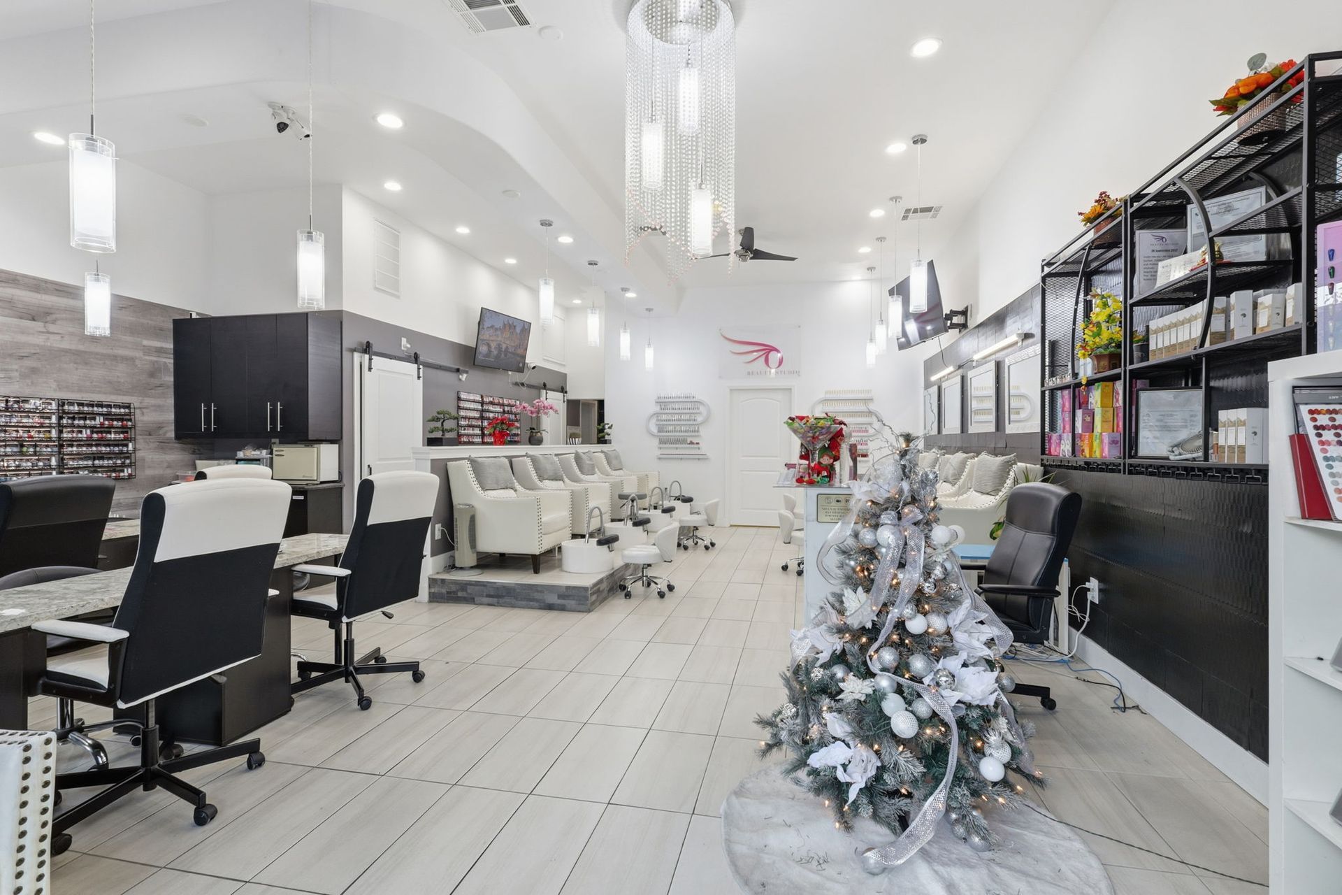 Interior of a nail salon with white and gray decor; several manicure and pedicure stations. Christmas tree.
