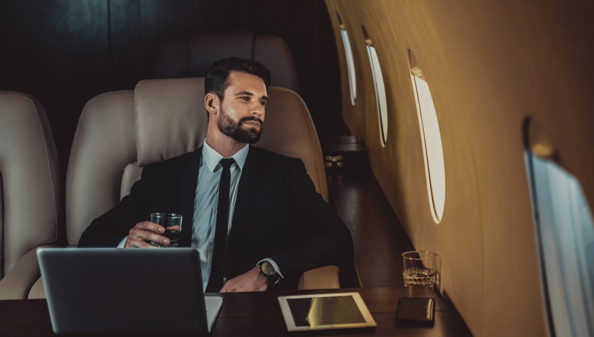 Un homme en costume est assis dans un jet privé avec un ordinateur portable et un verre de vin.